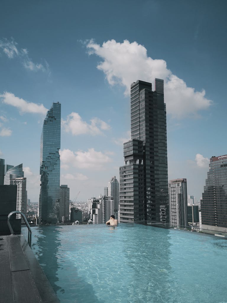A breathtaking rooftop pool offers a stunning view of Bangkok's modern skyline under clear skies.