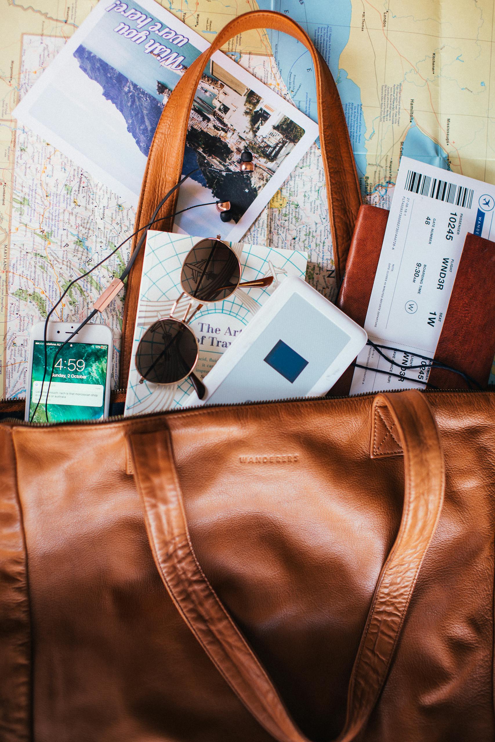 Flat lay of travel essentials including a leather bag map sunglasses and tickets